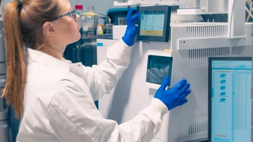 Female scientist adjusting settings on analytical laboratory equipment while wearing blue gloves and goggles
