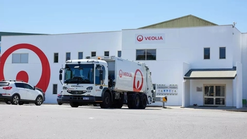 White Veolia branded refuse truck in front of a Veolia operations building with red logo signage on the wall