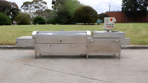 Stainless steel industrial machine on outdoor concrete with a green lawn and trees in the background