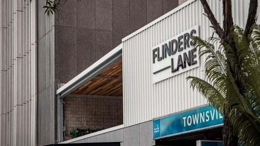 White building with Flinders Lane branding and a partial Townsville Enterprise sign with palm fronds visible